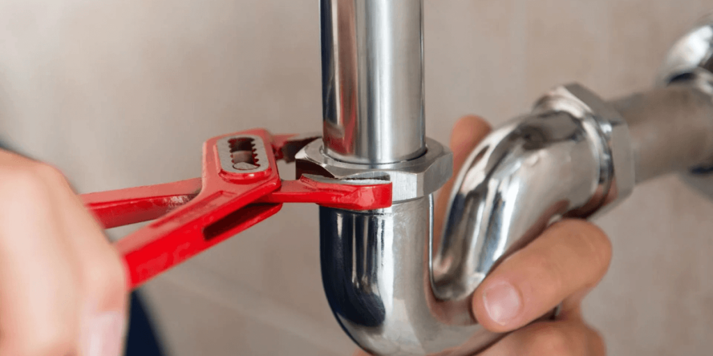 A person using a red tool to repair a pipe, demonstrating hands-on plumbing work.