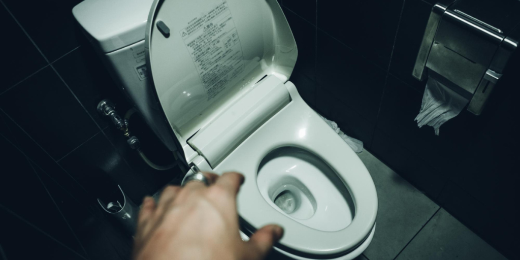 A person holding a toilet seat open, showcasing the interior of a restroom facility.